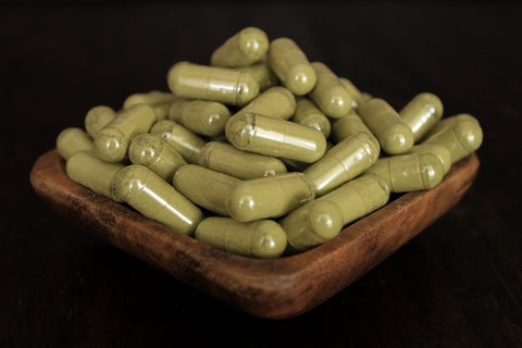 Green Jongkong powder in 1000 mg gelatin capsules in a wooden bowl
