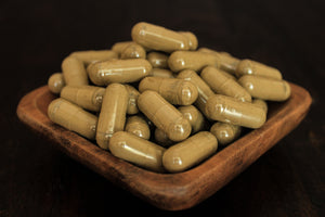 Natural red borneo fresh leaf powder in 1000 mg gelatin capsules presented in a wooden bowl