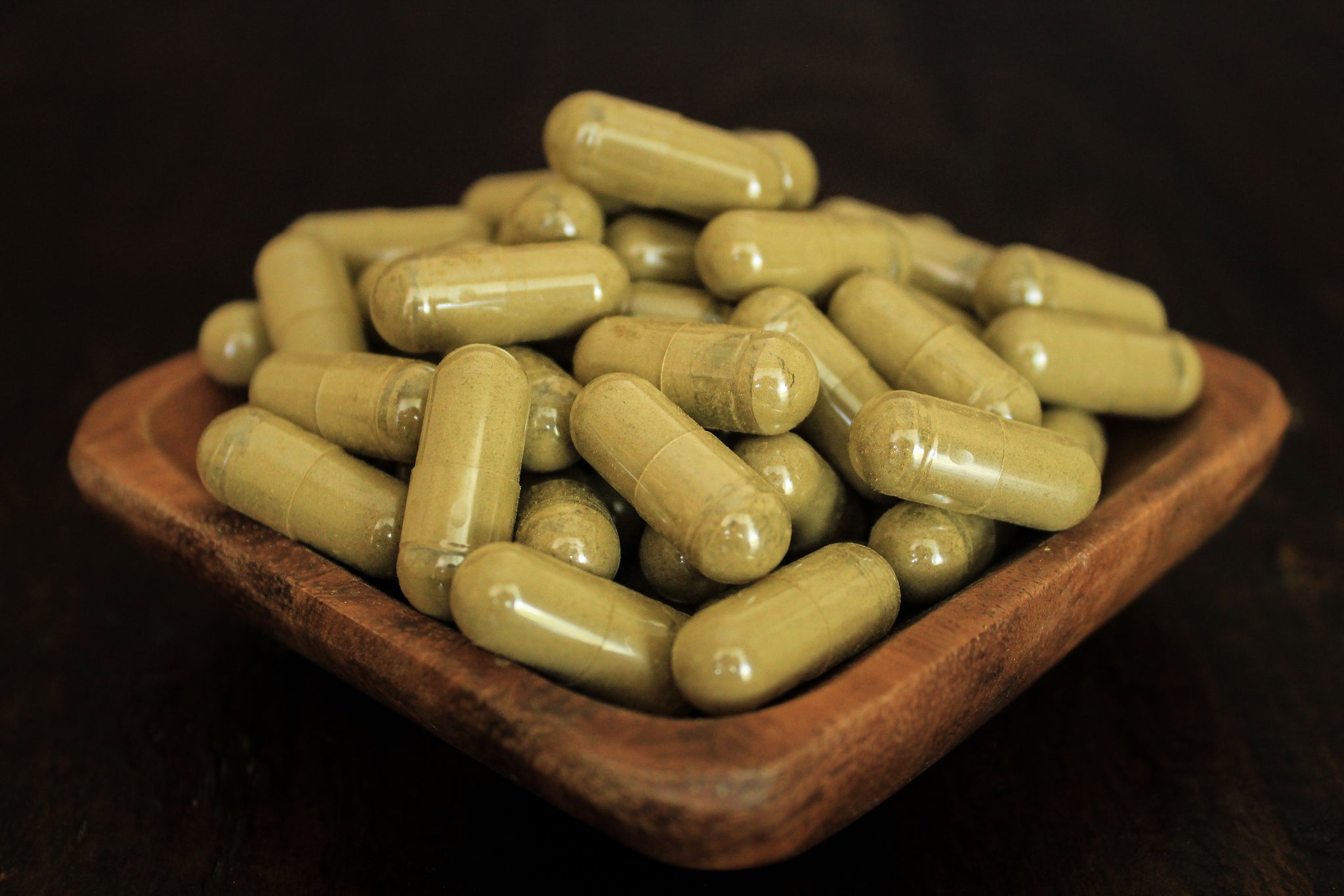 Super Red leaf powder in 1000 mg  gelatin capsules in a wooden bowl for close up