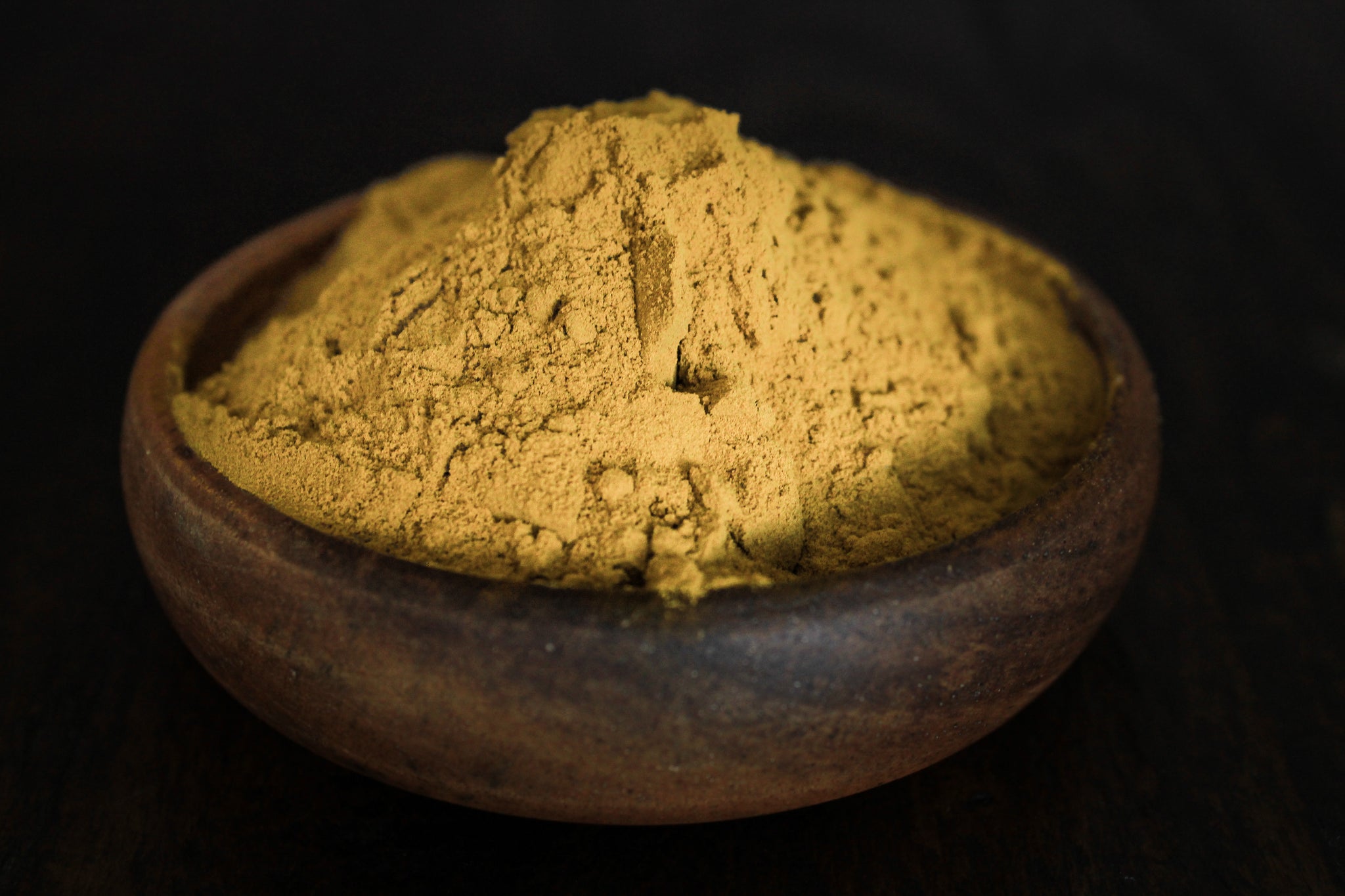 Fresh grinded yellow turmeric root powder shown in a wooden bowl